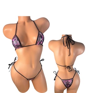 Może przedstawiać: Dwuczęściowy zestaw bikini z wzorem wężowej skóry w kolorze różowym, czarnym i fioletowym. Top bikini ma trójkątny krój z ramiączkami na szyję, a dół to stringi z wiązaniami po bokach. Zestaw jest prezentowany na manekinie.