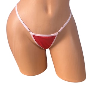 Peut inclure: String rouge avec bordures et bretelles blanches. Le sous-vêtement a un panneau avant triangulaire et une fine ceinture. Le vêtement est présenté sur un mannequin.