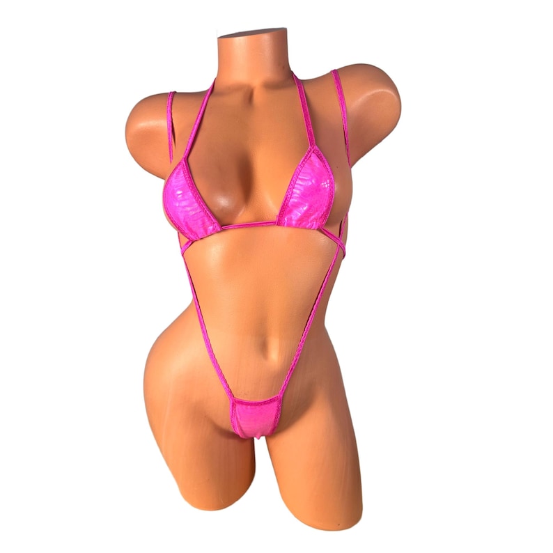 May include: A bright pink bikini set with a halter top and a thong bottom. The fabric has a textured, shiny appearance. The swimwear is displayed on a mannequin against a white background.