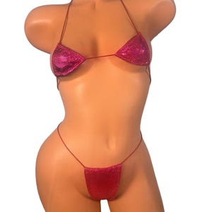 Può includere: Un bikini a due pezzi fucsia. Il top è a triangolo, e lo slip è a perizoma. Entrambi i pezzi sono ricoperti di paillettes scintillanti. Il bikini è esposto su un manichino.