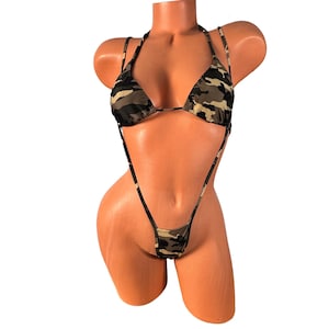 May include: A camouflage print bikini set. The top is a triangle style with halter straps. The bottom is a thong style with a high-cut leg. The fabric has a pattern of green, brown, and tan.