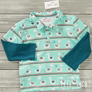 May include: A long-sleeved polo shirt with a turquoise background and a pattern of white llamas, yellow and red stripes, and small floral accents. The sleeves are a solid teal color. The tag reads "PETE + LUCY".