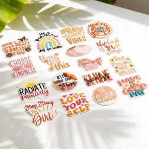 May include: A collection of embroidered patches with positive affirmations and phrases. The patches feature various colors and designs, including rainbows, suns, and floral elements. Text includes "Spread Good Vibes", "Choose Kindness", and "Radiate Positivity".