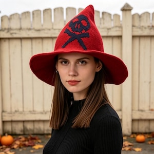 May include: A bright red pointed hat with a wide brim, featuring a dark navy blue skull and crossbones graphic knitted into the front center. The hat has a textured, woven appearance and a structured, slightly conical shape that tapers to a point.