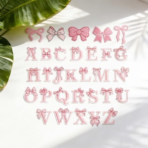 May include: A collection of pink embroidered alphabet letters and bow patches. The letters A to Z are shown, each with a bow detail. Several bow patches in different shades of pink are also present. These patches are likely for crafting or customisation projects.