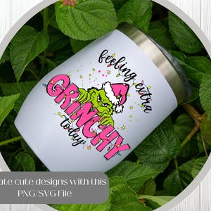May include: A white insulated tumbler with a stainless steel rim features a Grinch design in pink and green, with the words "feeling extra Grinchy today." The tumbler is surrounded by green foliage.