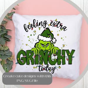 May include: White square pillow with a Grinch design. The Grinch is green and wearing a Santa hat. The words "feeling extra GRINCHY today" are written on the pillow in black and green. The design includes Christmas lights and stars.