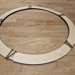 Könnte beinhalten: Ein runder, unfertiger Holzkreis mit vier Metallklammern am Rand. Der Kreis liegt flach auf einer Holzoberfläche.