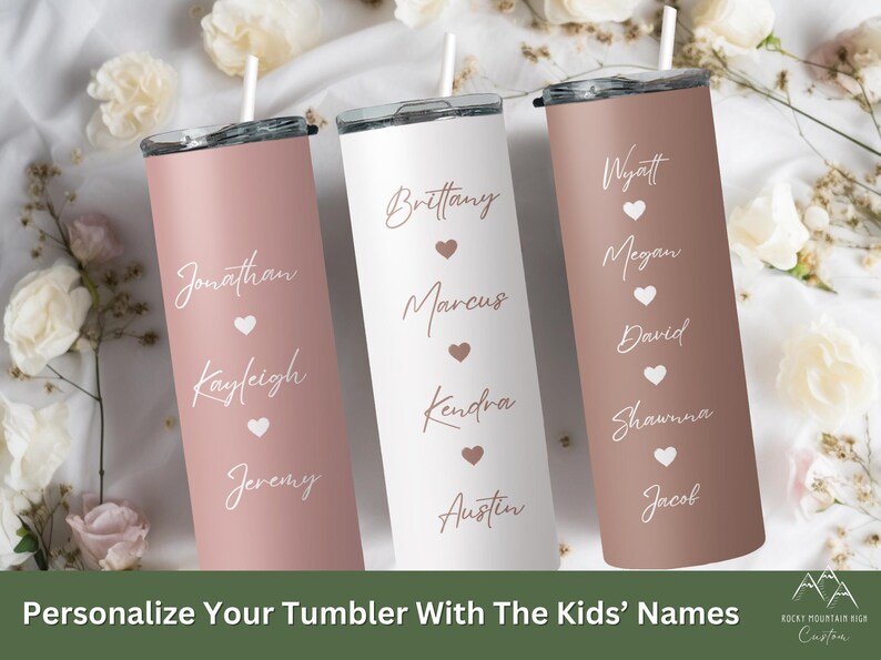 May include: Three personalized stainless steel tumblers with pink, white, and brown finishes. Each tumbler features a name and heart design. The tumblers are arranged in a row on a white surface with flowers in the background. The text on the tumblers reads: "Brittany, Marcus, Kendra, Austin", "Jonathan, Kayleigh, Jeremy", and "Wyatt, Megan, David, Shawna, Jacob".