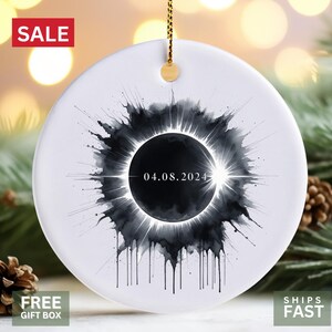 May include: White ceramic ornament with a black and white watercolor illustration of a solar eclipse with the date 04.08.2024.