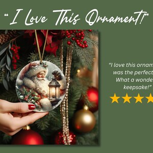 Puede incluir: Un adorno navide&ntilde;o redondo de cer&aacute;mica con una ilustraci&oacute;n detallada de Santa Claus sosteniendo una linterna brillante. El texto "I Love This Ornament!" aparece en la parte superior, y una rese&ntilde;a de cinco estrellas con el texto "I love this ornament! It was the perfect gift. What a wonderful keepsake!" se muestra junto al adorno.