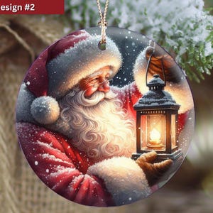 Puede incluir: Un adorno navide&ntilde;o redondo de cer&aacute;mica con una ilustraci&oacute;n detallada de Santa Claus con una larga barba blanca, vistiendo un traje rojo con ribete de piel blanca, sosteniendo una linterna negra con una luz brillante sobre un fondo nevado.