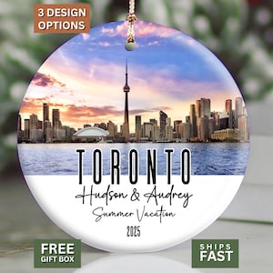 May include: Round ceramic ornament featuring a Toronto skyline at sunset. The ornament includes the text "TORONTO", "Hudson & Audrey", "Summer Vacation 2025". The ornament has a gold string for hanging.