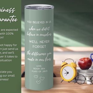 May include: A sage green tumbler with a silver lid, inscribed with white text. The text reads, "You believed in us... We'll never forget the difference you made in our lives." A yellow alarm clock, apple, and glasses are next to the tumbler.