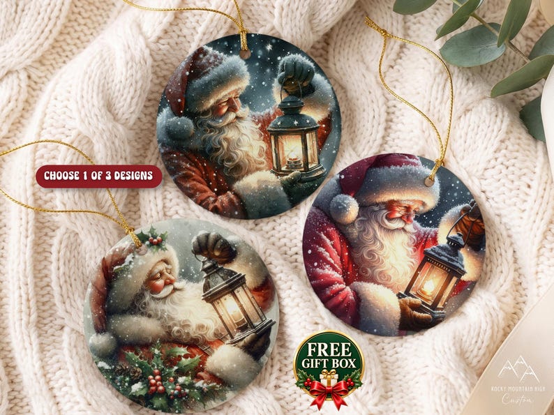 Puede incluir: Tres adornos navide&ntilde;os redondos de cer&aacute;mica con ilustraciones de Santa Claus sosteniendo una linterna brillante. Cada adorno tiene un cord&oacute;n dorado. El texto CHOOSE 1 OF 3 DESIGNS y FREE GIFT BOX es visible en la imagen.
