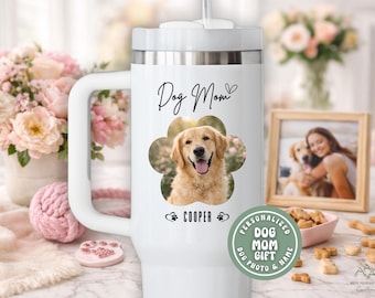 May include: White travel mug with a handle, featuring a photo of a golden retriever in a flower-shaped frame. The text "Dog Mom" and the dog's name "Cooper" are also displayed. A small photo frame and dog treats are in the background.