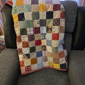 May include: A patchwork quilt constructed from numerous square fabric pieces in a variety of colors and patterns, including floral, plaid, paisley, and solid prints. The quilt features visible white yarn ties at the corners of each square.