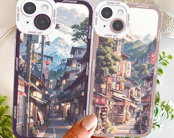 Może przedstawiać: Dwa etui na telefon z japońskim wzorem anime. Etui przedstawiają szczegółową ilustrację tradycyjnej japońskiej sceny ulicznej z budynkami, drzewami i górami. Etui są oznaczone jako "ANIME ART" i "JAPANESE".