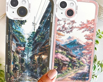 Może przedstawiać: Dwa etui na telefon z japońską grafiką anime. Jedno etui ma zieloną obwódkę i przedstawia scenę uliczną. Drugie etui ma różową obwódkę i przedstawia krajobraz górski z kwiatami wiśni. Oba etui mają napis "ANIME ART" i "JAPANESE".