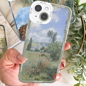 May include: Clear phone case featuring a Claude Monet painting of a landscape with a field of red flowers. The case has a green border with the text "CLAUDE MONET" and "ART LIFE" printed on it. The phone's camera is visible.