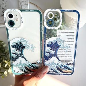 May include: Two phone cases featuring the iconic "Great Wave off Kanagawa" artwork by Katsushika Hokusai. The cases have a clear border with the text "ART LIFE" and "THE GREAT WAVE". The artwork depicts a large wave with a boat.