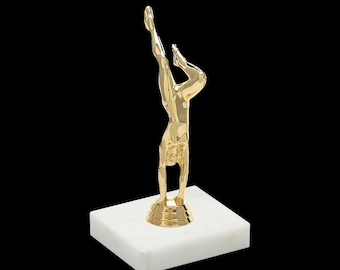 May include: Gold-colored trophy of a person doing a handstand on a white marble base.