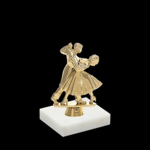 May include: A gold-colored trophy featuring a couple dancing. The couple is standing on a round base, which is mounted on a white marble square base.