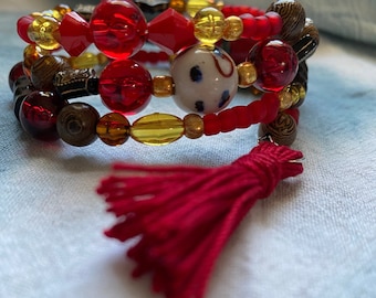 red wrap bracelet with ochre and golden tones, includes a tassel, and glass beads