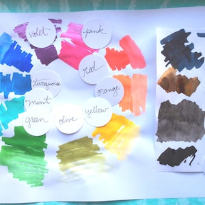May include: A color wheel with swatches of paint in various colors, including blue, violet, turquoise, mint, green, olive, yellow, orange, red, pink, and blue-black. The colors are labeled with their names in white circles.