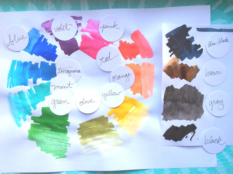 May include: A color wheel with swatches of paint in various colors, including blue, violet, turquoise, mint, green, olive, yellow, orange, red, pink, and blue-black. The colors are labeled with their names in white circles.