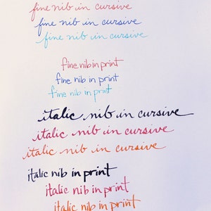 May include: A close-up of a white surface with handwritten text in different colors. The text reads "fine nib in cursive", "italic nib in cursive", and "fine nib in print".
