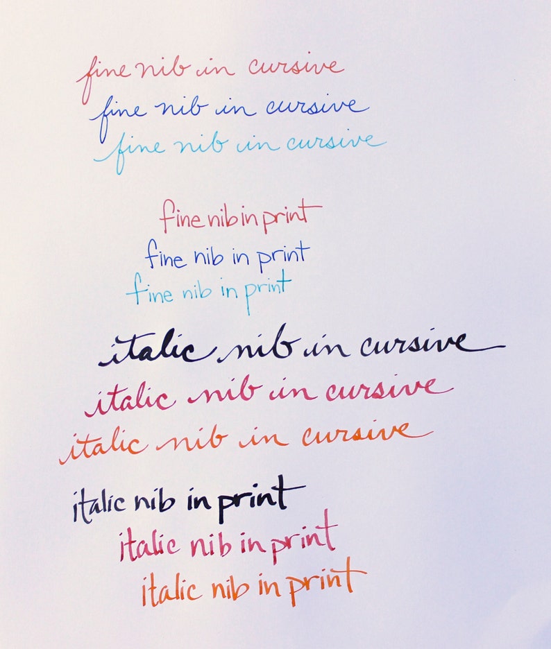 May include: A close-up of a white surface with handwritten text in different colors. The text reads "fine nib in cursive", "italic nib in cursive", and "fine nib in print".