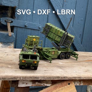 Puede incluir: Maqueta detallada de un vehículo militar en tonos verdes, con el texto "SVG • DXF • LBRN" en blanco. El modelo se encuentra sobre un fondo de madera azul desgastada, mostrando un diseño y construcción intrincados.