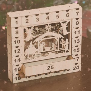 Light-colored wooden nativity advent calendar with number 25 drawer slightly open, surrounded by wrapped gifts.