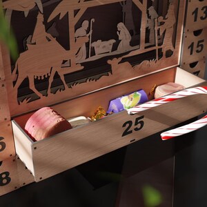 Close-up of the pulled-out bottom drawer number 25 of a wooden advent calendar, revealing various candies and a candy cane.