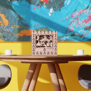 Light wooden nativity advent calendar centered on a wooden dining table between two chairs against a colorful painted wall.