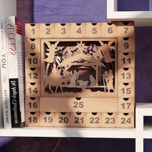 Light wooden nativity advent calendar positioned on a white shelving unit beside books.