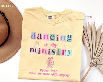 May include: A light yellow t-shirt with the words "dancing is my ministry" in colorful block letters. The shirt also features a ballet shoe graphic and the text "Psalm 149:3 Praise his name with dancing."