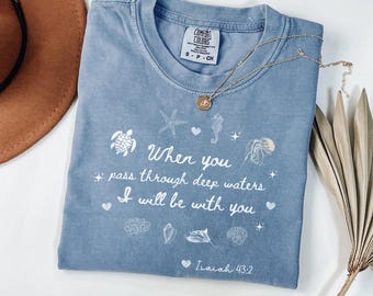 May include: A light blue t-shirt with a white design featuring a seashell, starfish, turtle, and a quote from Isaiah 43:2, "When you pass through deep waters I will be with you."