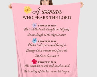 May include: A pink throw blanket with the text "A woman who fears the Lord" and bible verses from Proverbs 31:25, 31:30, and 31:26. The blanket features floral illustrations.