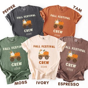 May include: Five short-sleeve crew neck t-shirts in pepper, yam, moss, ivory, and espresso colors. Each shirt features a graphic of a wagon carrying a pumpkin and flowers, with the text "FALL FESTIVAL CREW 2026" printed in a distressed font.