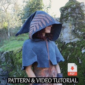 May include: A dark blue hooded cloak with a fern design on the hood. The cloak has a matching cape and a brown tie closure. The image also includes the text "PATTERN & VIDEO TUTORIAL".