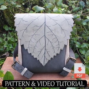 May include: A gray leather bag with a leaf design on the front flap. The bag has two straps and a buckle closure. The bag is sitting on a wooden surface.  PATTERN & VIDEO TUTORIAL PDF