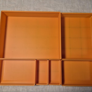 May include: A set of five orange plastic storage containers with lids. The containers are nested inside each other, with the largest container at the bottom and the smallest container at the top.