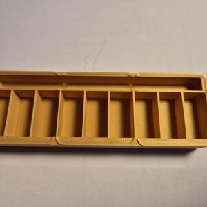 May include: A rectangular, gold-coloured plastic storage box with ten compartments. The box is empty.