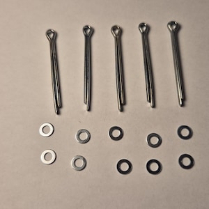 May include: Six silver metal cotter pins and twelve silver metal washers. The cotter pins are approximately 2.5 cm long and the washers are approximately 1.25 cm in diameter.