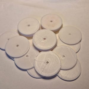May include: A pile of white plastic discs with a small hole in the centre of each disc. The discs are stacked on top of each other.