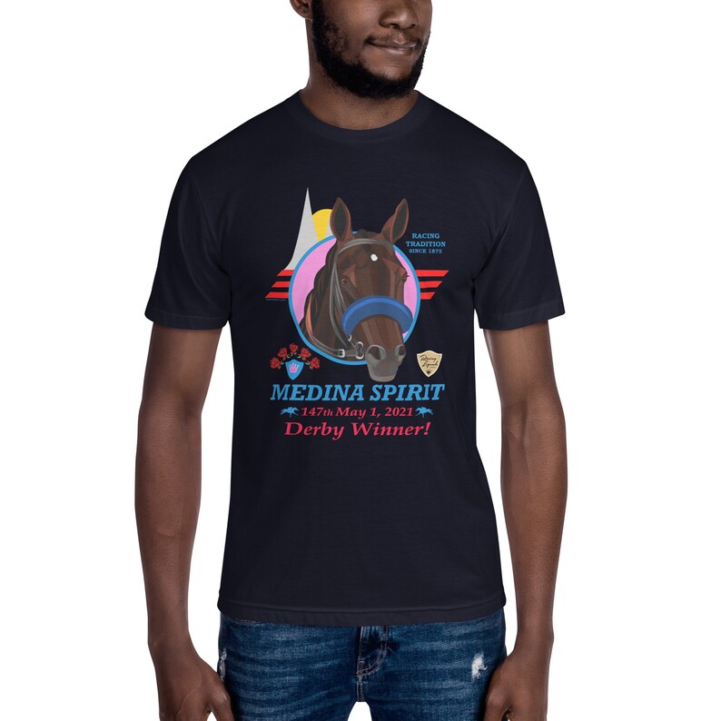 Puede incluir: Camiseta azul marino con un gr&aacute;fico de cabeza de caballo, brida azul y c&iacute;rculo rosa. El texto "MEDINA SPIRIT Derby Winner!" est&aacute; debajo. Tradici&oacute;n de carreras desde 1875.