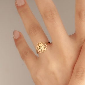 Pode incluir: Um anel de ouro com um design geométrico. O anel está em um dedo.