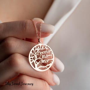 May include: A rose gold necklace with a circular pendant featuring a tree design with the names "Dorothee", "Lina", and "Brice" inscribed on the branches.